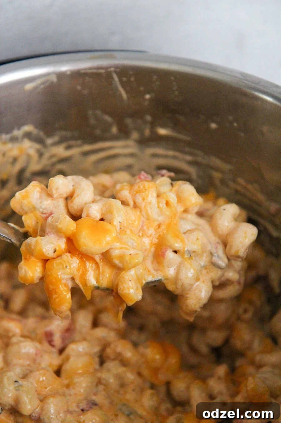 A generous spoonful of creamy mac and queso being lifted from the Instant Pot, showing the rich, melted cheese and pasta.