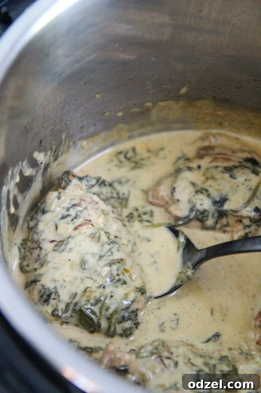 Creamy Tuscan chicken in an Instant Pot with a black serving spoon, showcasing the rich texture of the sauce.