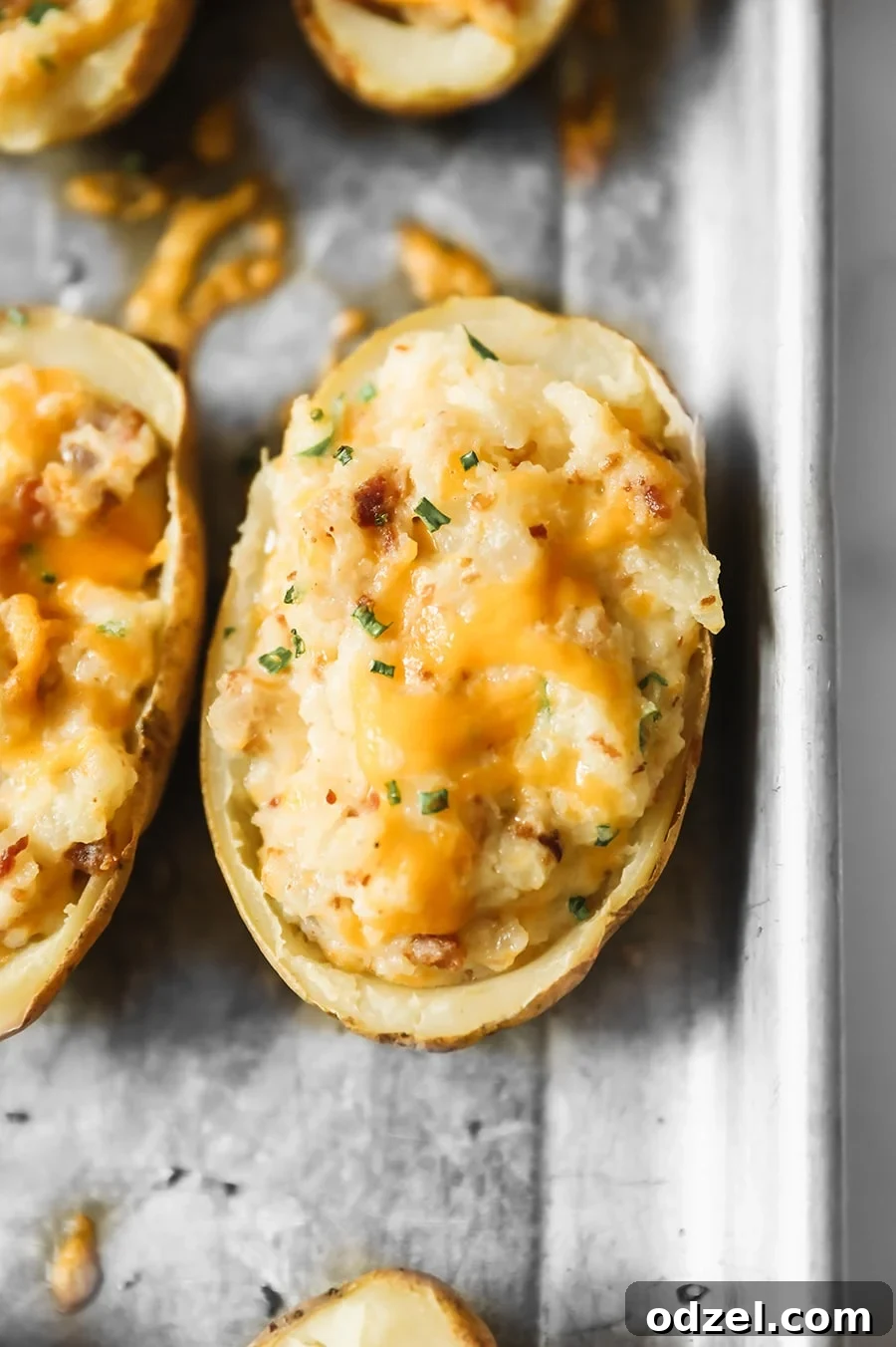 Ultimate Stuffed Potatoes 2 Two golden-brown twice baked potatoes, generously topped with melted yellow cheddar cheese and fresh green chives, served on a rustic white plate.