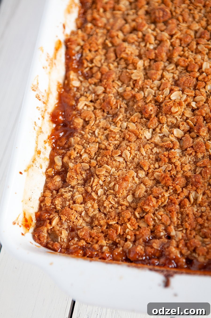 A close-up view of a baked apple crisp, showcasing the golden, crumbly oat topping and the bubbling, tender apple filling underneath.