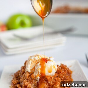 A spoon drizzling caramel sauce over apple crisp with vanilla ice cream on a white plate, highlighting its delicious appeal.