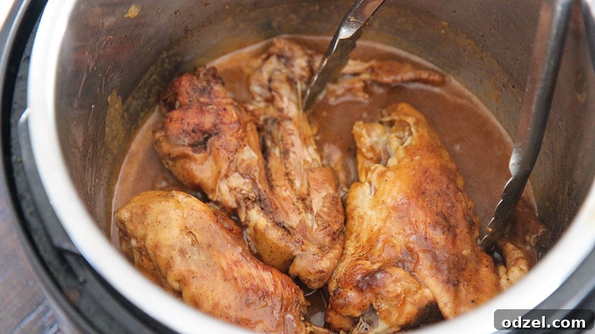 three smothered turkey wings in the instant pot with a pair of tongs, ready to be served.