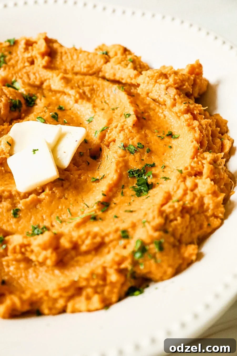 Mashed sweet potatoes with melted butter and fresh green herbs on top, served in a rustic bowl.