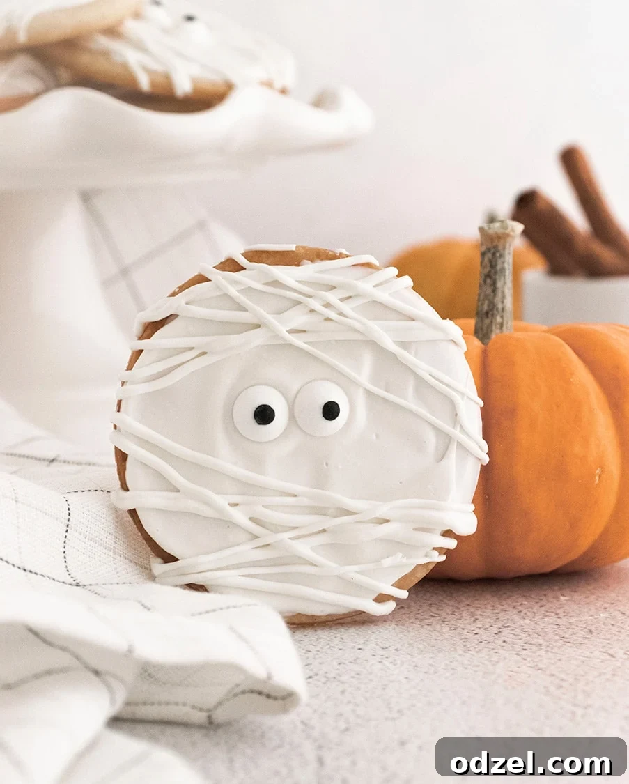A single decorated mummy cookie showcased next to a small orange decorative pumpkin, highlighting its spooky yet cute appearance and festive charm.