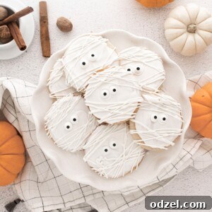Mummy cookies on a white plate with decorative pumpkins on the side, showcasing a delicious and festive Halloween treat.