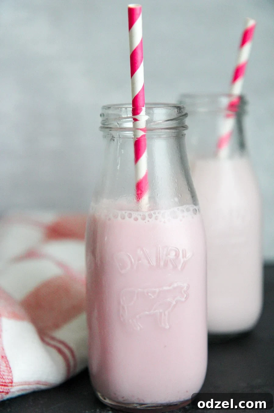 Sweet Berry Milk Infusion 2 Two milk jugs filled with vibrant pink homemade strawberry milk, adorned with fun pink and white straws, standing on a light surface.