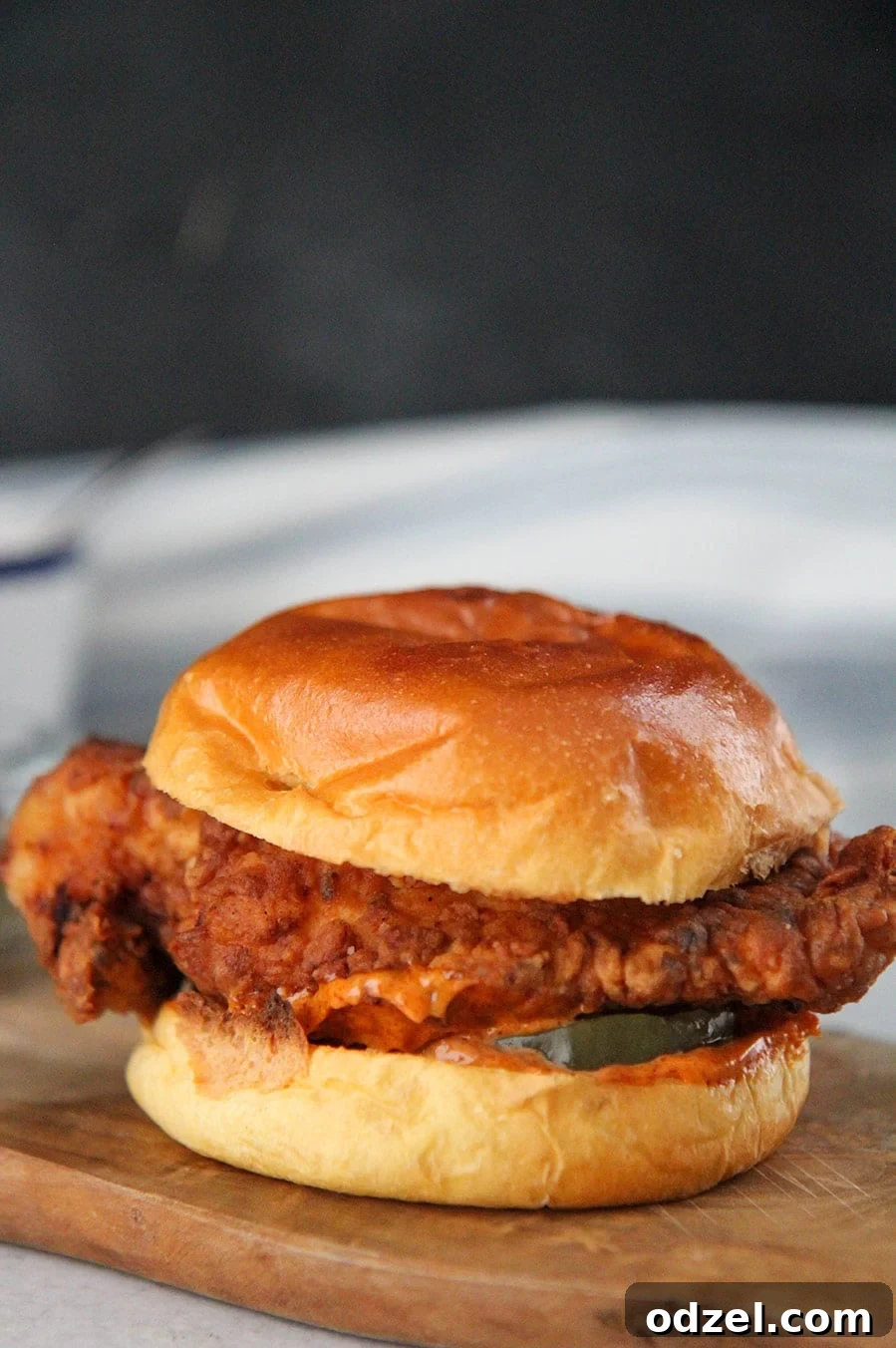 A perfectly fried Popeyes-style chicken sandwich on a wooden board, garnished with pickles.