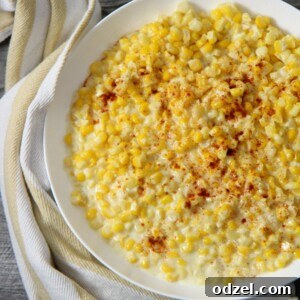 creamed corn in a white plate with a yellow and white kitchen towel on the side.