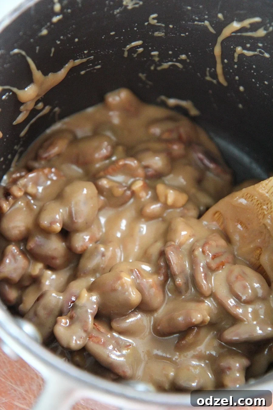 A black saucepan filled with the warm, rich pecan praline mixture, with a wooden spoon resting inside.