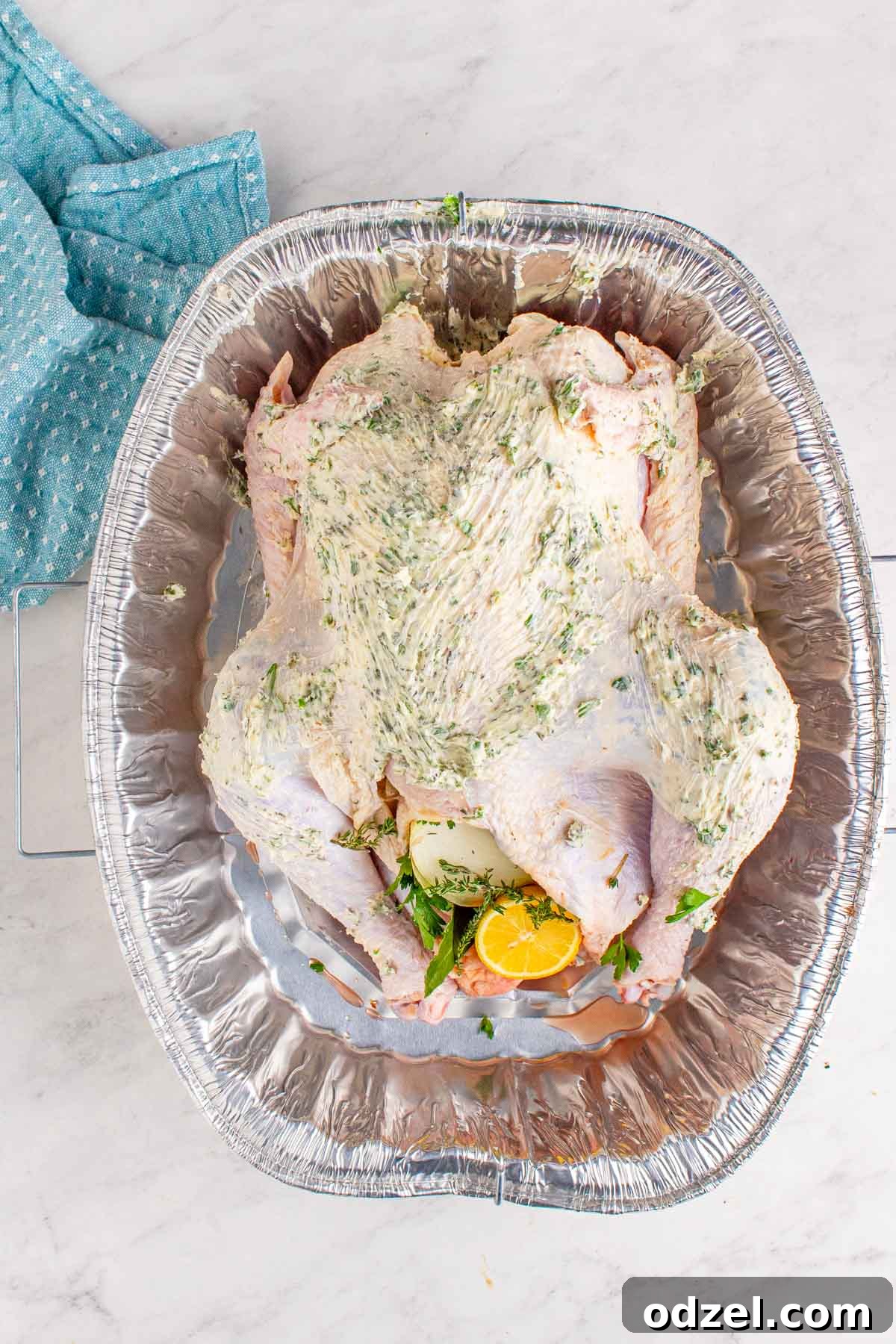 raw turkey smothered with softened butter and herbs inside a baking dish. 