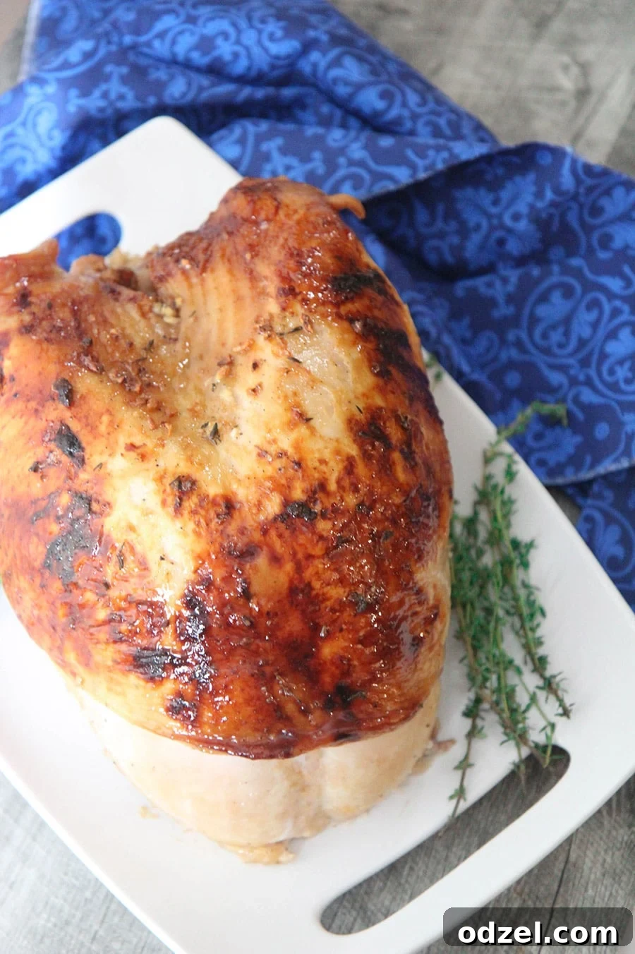 Golden Maple Glazed Turkey Breast 2 A perfectly roasted maple glazed turkey breast on a white platter, garnished with fresh thyme, resting on a blue kitchen towel.
