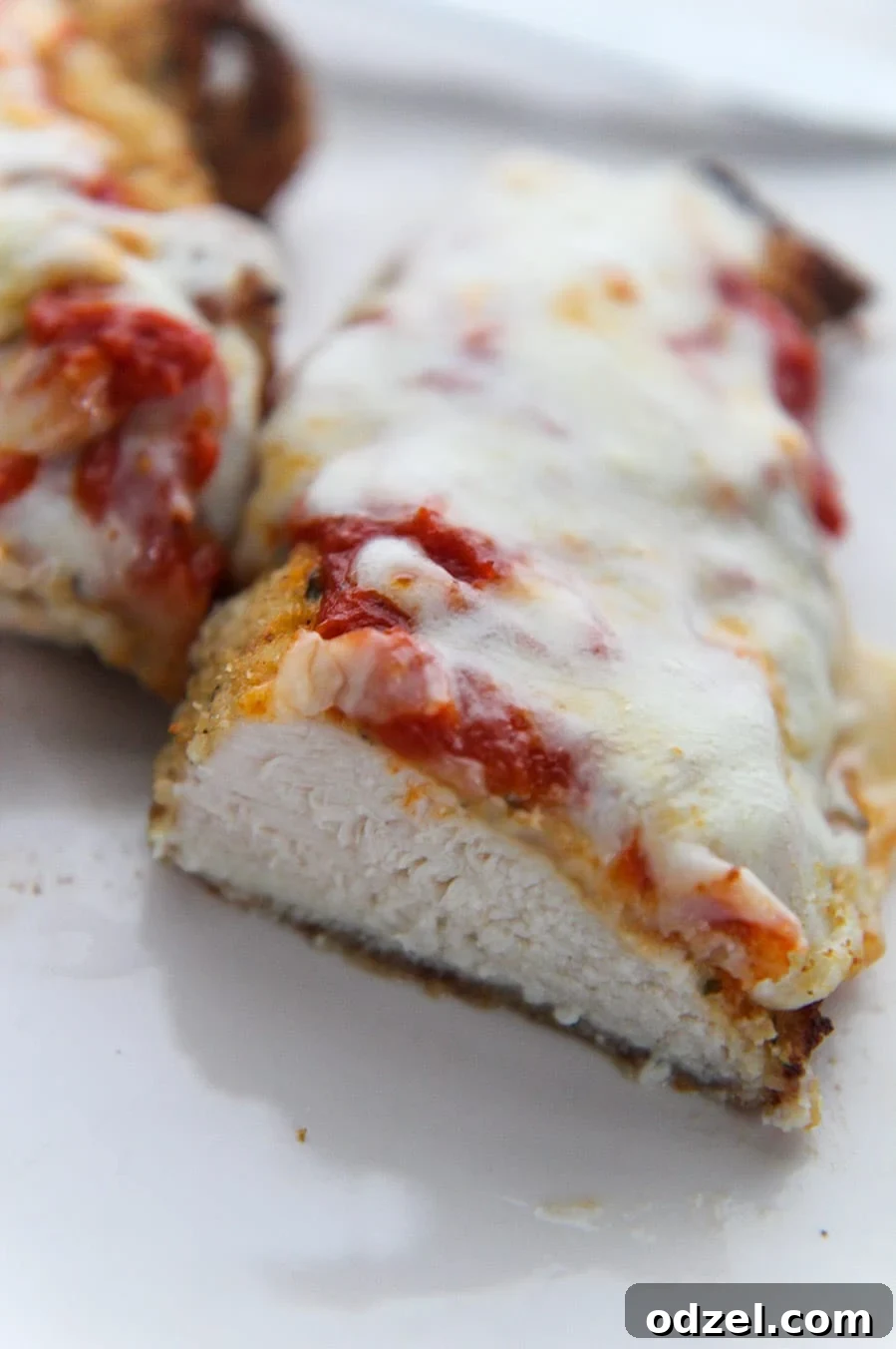 A cooked chicken parmesan sliced in half, revealing the juicy chicken, melted cheese, and marinara sauce inside.