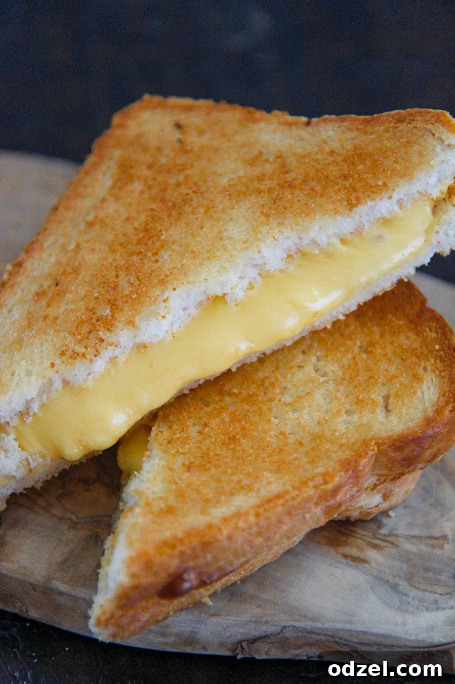 two grilled cheese sandwiches stacked on top of each other on a wooden board. 