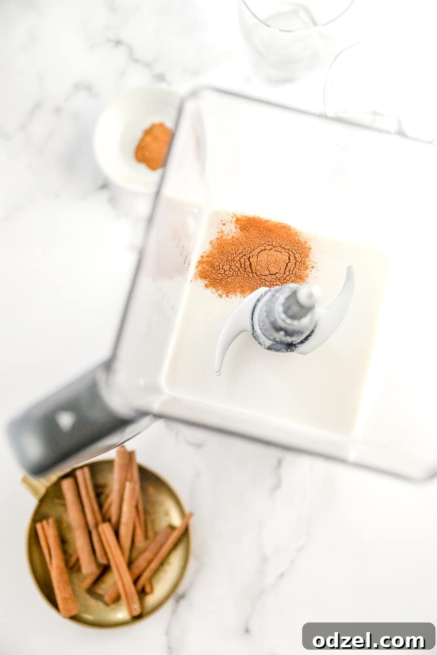 Ingredients for Coquito in a blender with cinnamon sticks on the side.