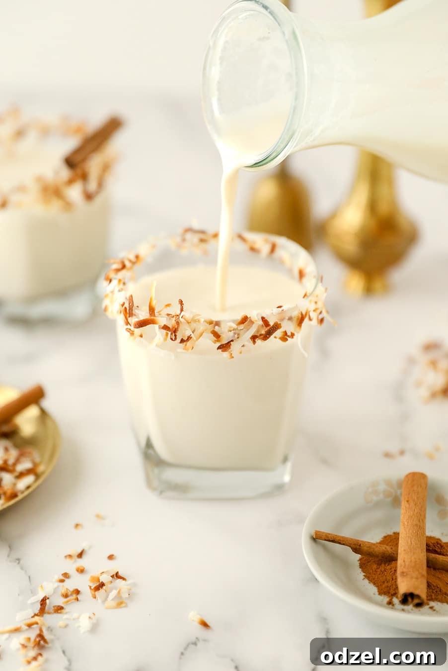 A milk jug pouring Coquito into a short glass.