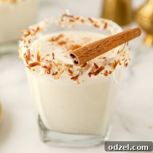 Coquito in a short glass with toasted coconut on the rim and a cinnamon stick on top.