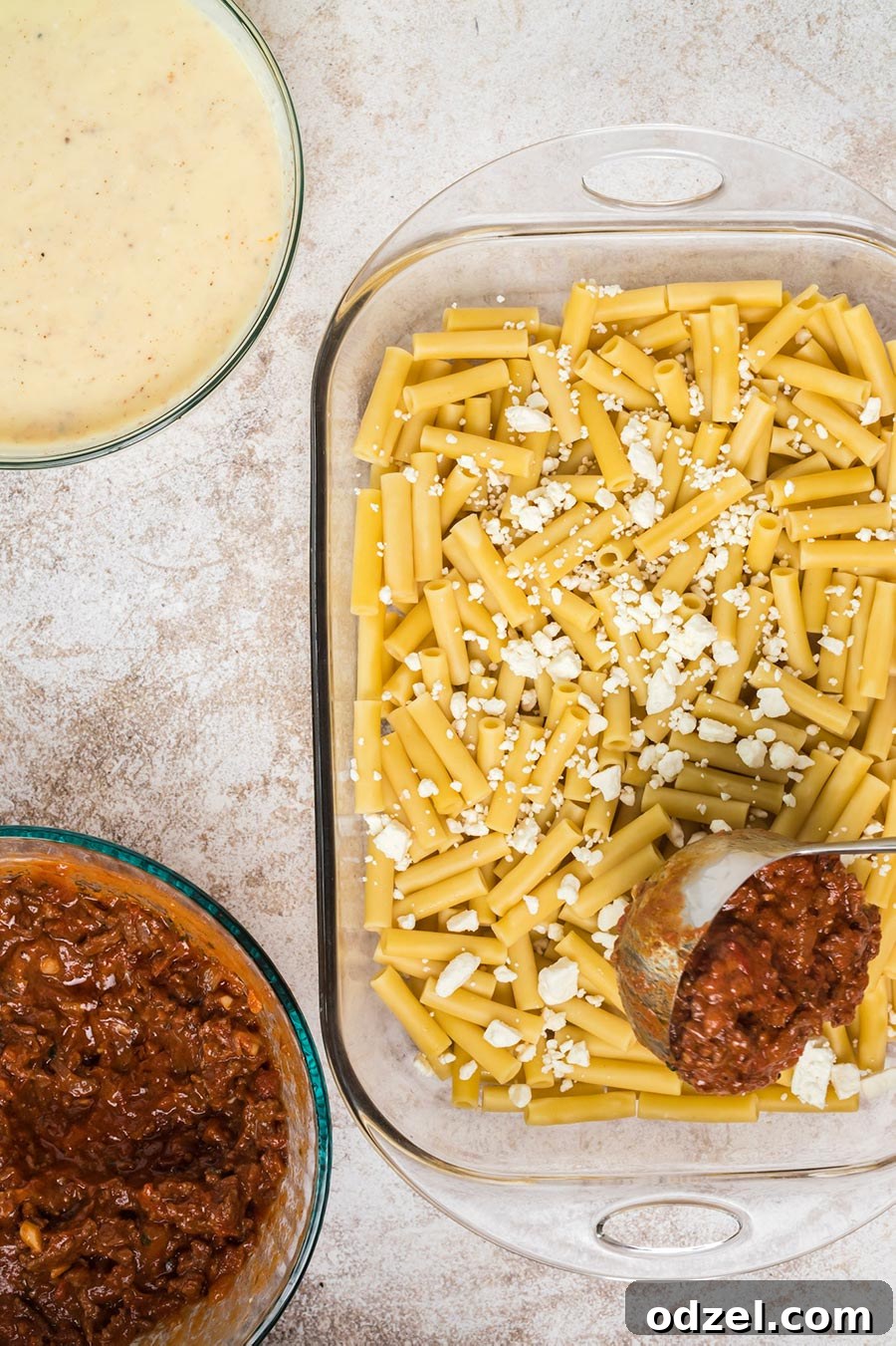 Cooked ziti pasta, a ladle of savory meat sauce, a bowl of rich béchamel sauce, and another bowl of meat sauce displayed for Pastitsio preparation.