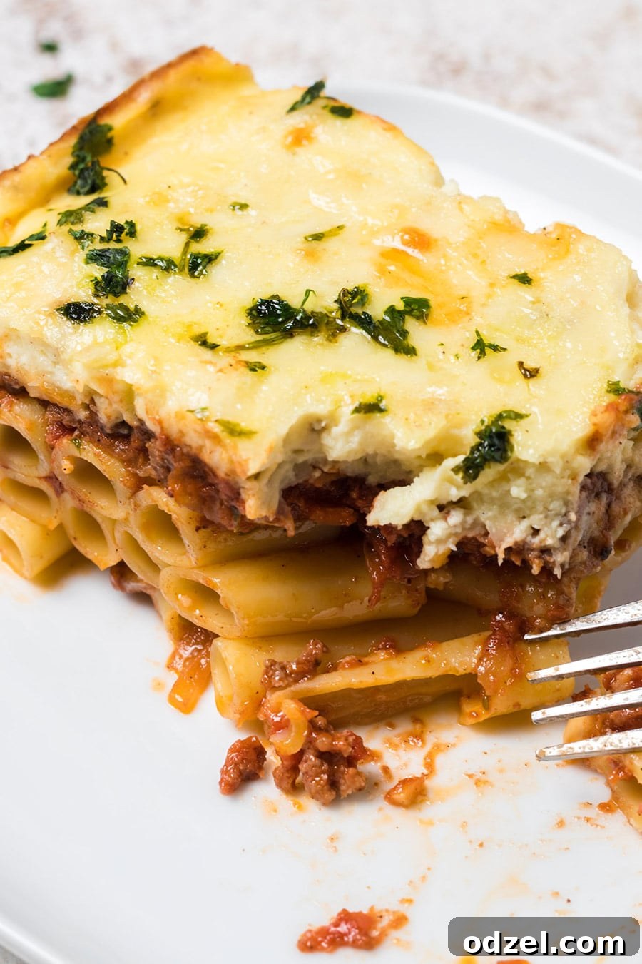 A perfectly portioned slice of Greek lasagna (Pastitsio) on a white plate with a fork resting beside it.
