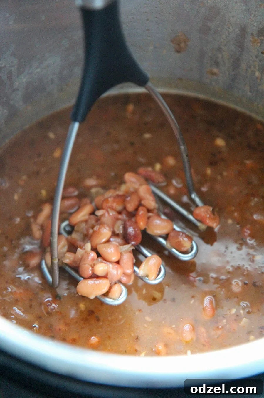 Creamy Instant Pot Refried Beans 3 Cooked pinto beans in the Instant Pot with a potato masher resting inside, ready for mashing.