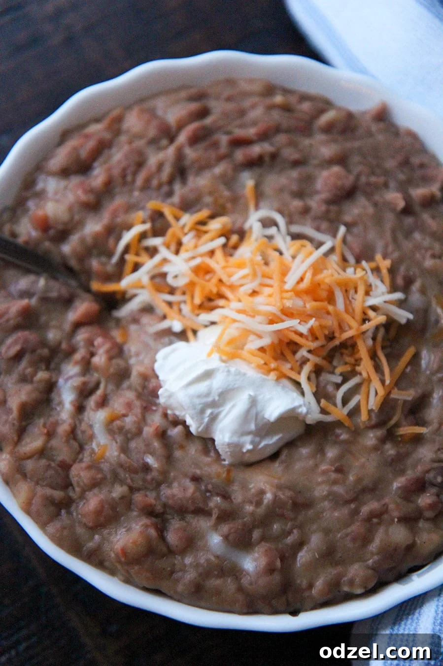 Creamy Instant Pot Refried Beans 4 Close-up of creamy refried beans topped with a generous amount of sour cream and melted shredded cheese in a white bowl.