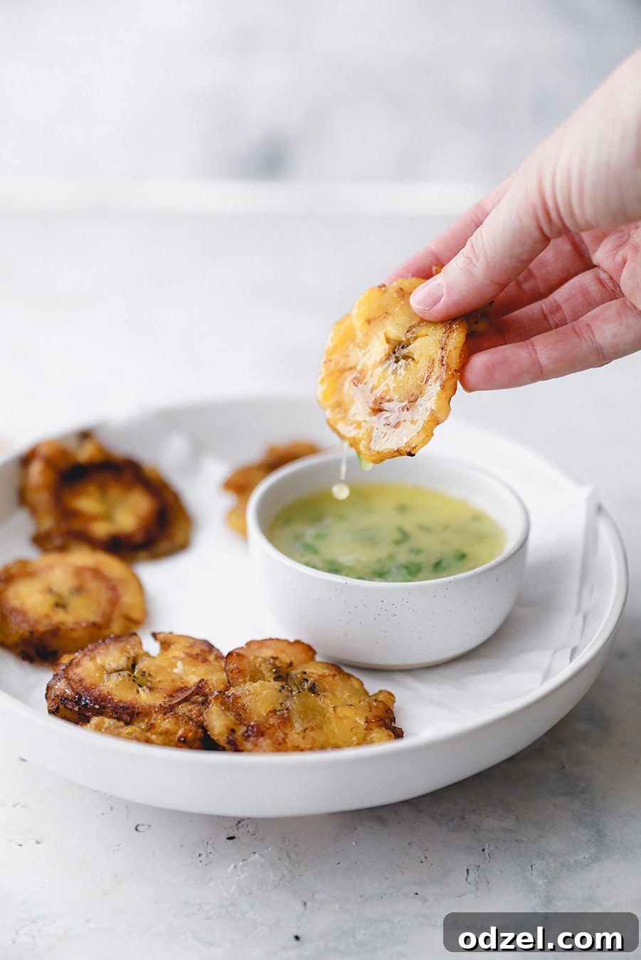 A single crispy toston being dipped into a small bowl of savory garlic butter sauce, highlighting its golden texture.