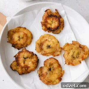 Six tostones on a white plate with a side of garlic butter sauce, ready to be enjoyed.