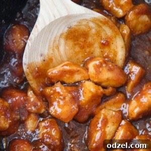 Tangy Orange Crock-Pot Chicken 4 Orange chicken cooking in the slow cooker with a wooden spoon.