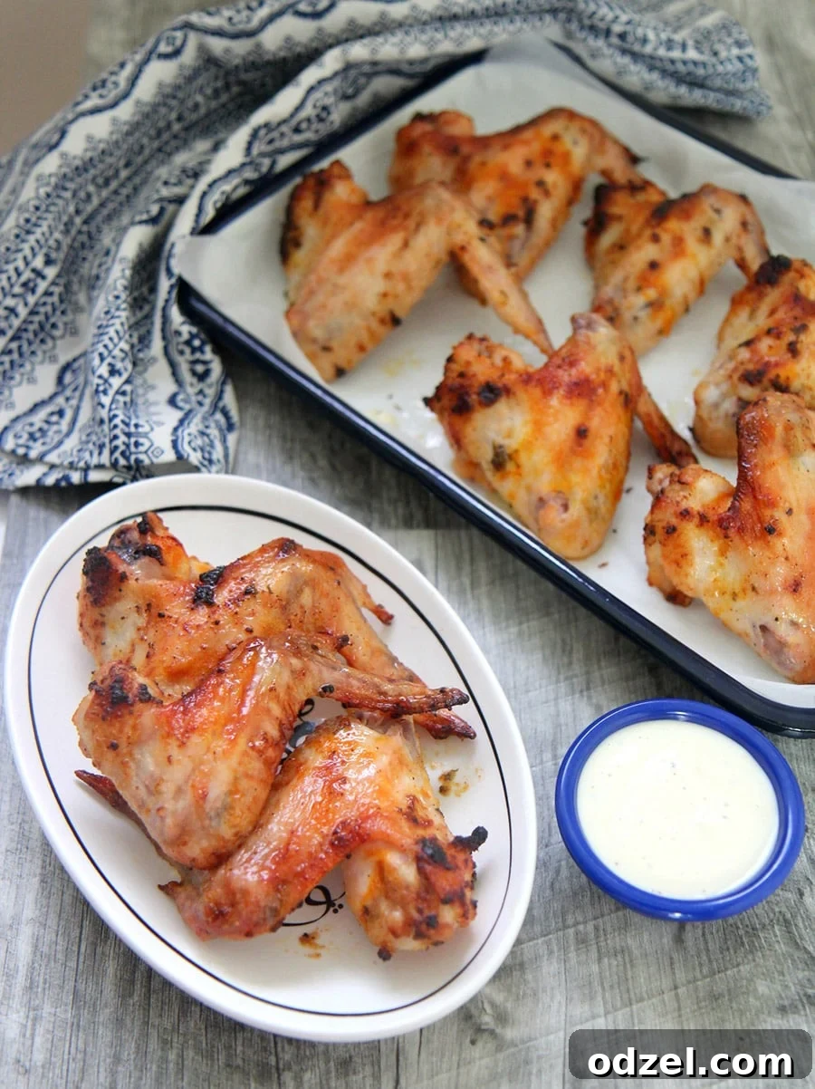 Crispy oven roasted chicken wings on a small white plate with a side of blue cheese dip and more wings in the background, ready to be served.