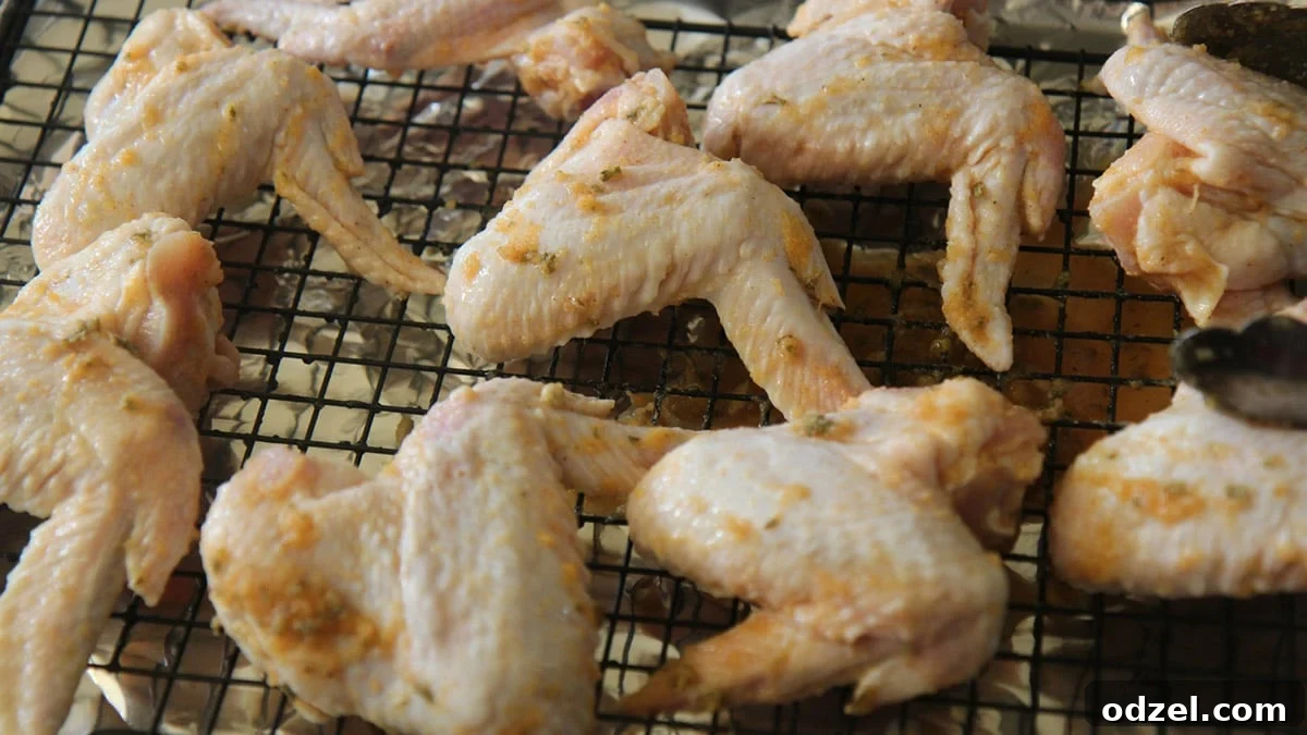Raw chicken wings marinated in lemon butter mixture, arranged on a baking sheet with a wire rack, ready for oven roasting.