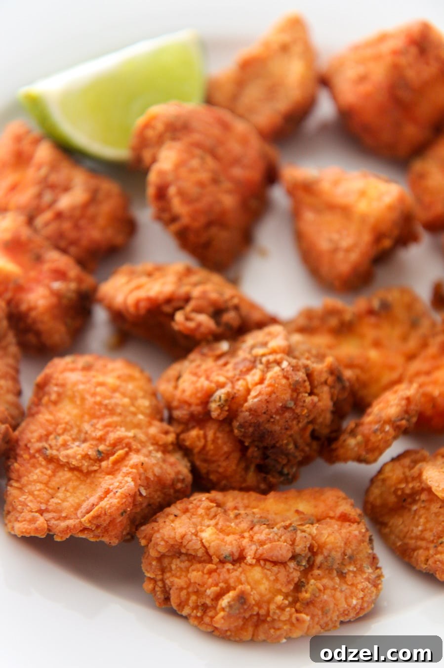 Close-up view of golden-brown crispy fried Chicharron de Pollo bites, garnished with a fresh lime wedge, highlighting their crunchy texture.