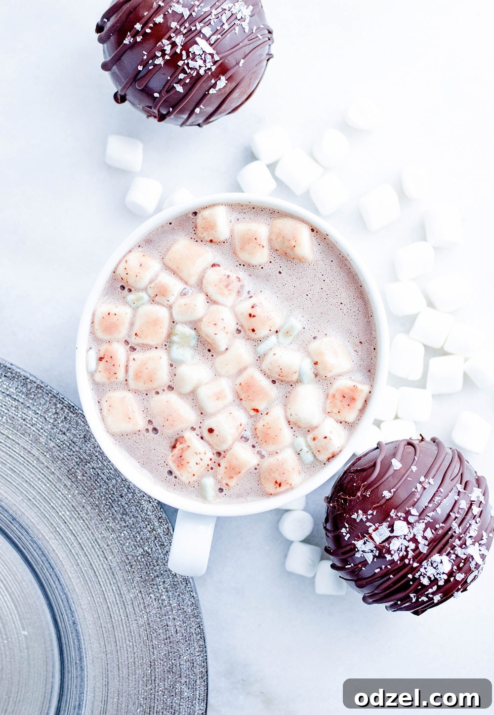 A cozy mug filled with steaming hot cocoa, topped with a cloud of mini marshmallows, positioned next to two irresistible salted caramel hot cocoa bombs, inviting you to indulge in a warm winter moment.