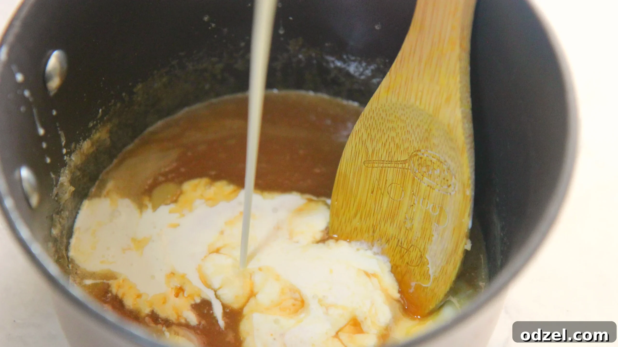 Decadent Sea Salt Caramel Cheesecake 4 Caramel sauce and heavy cream in a saucepan with a wooden spoon, illustrating the sauce-making process.