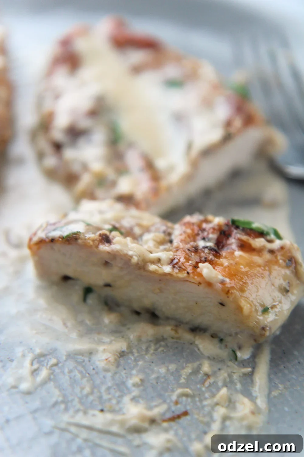 A sliced piece of creamy garlic parmesan chicken on a gray plate, ready to be served.