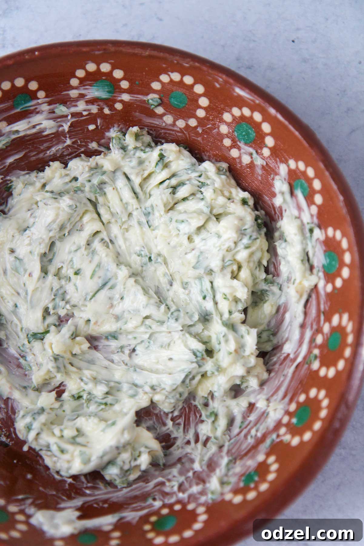 close up of a bowl containing a mixture of softened butter, minced garlic, and fresh parsley, ready to be spread.
