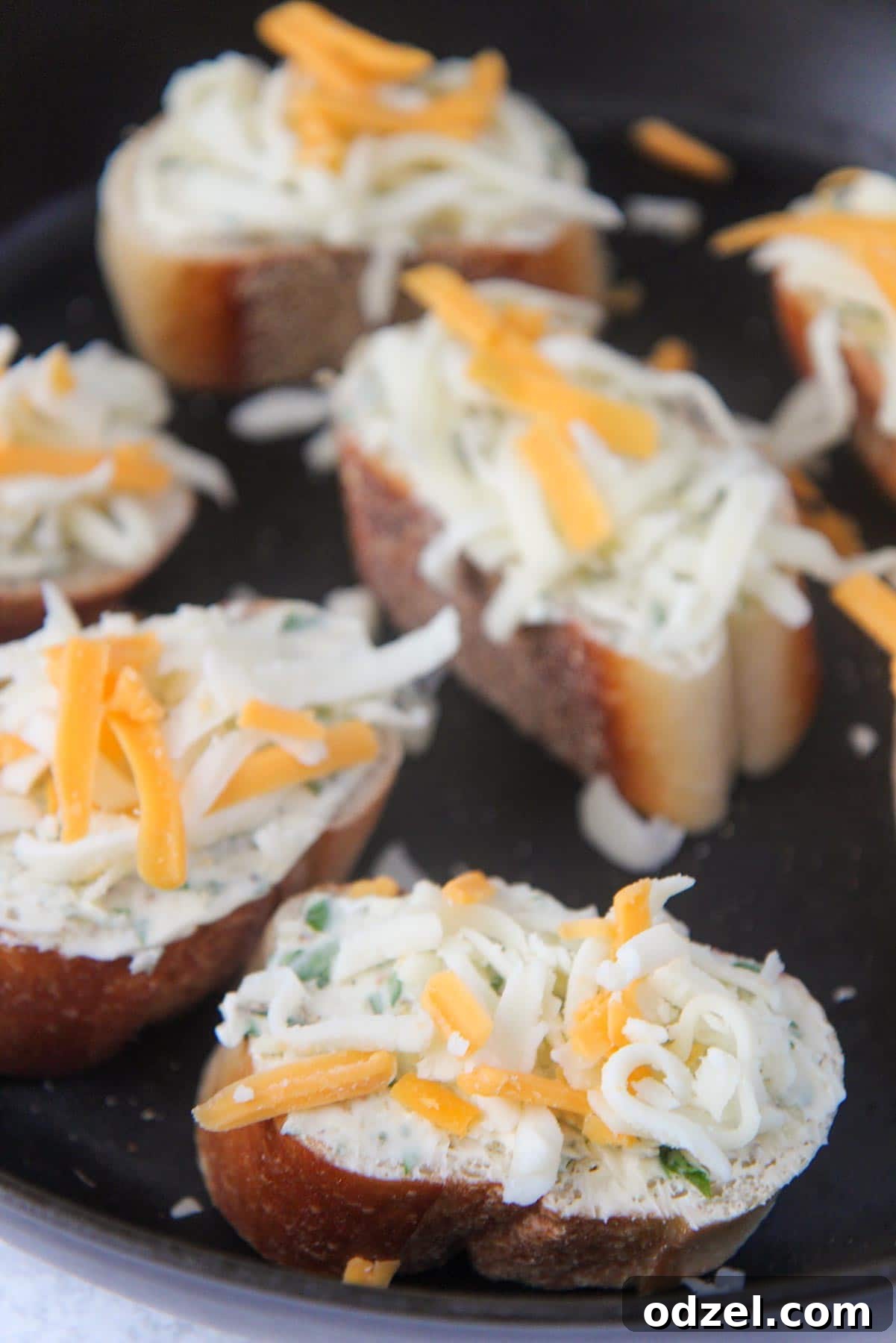 two halves of French bread, generously buttered and topped with mozzarella, cheddar cheese, and oregano, placed on a baking sheet, ready for baking.