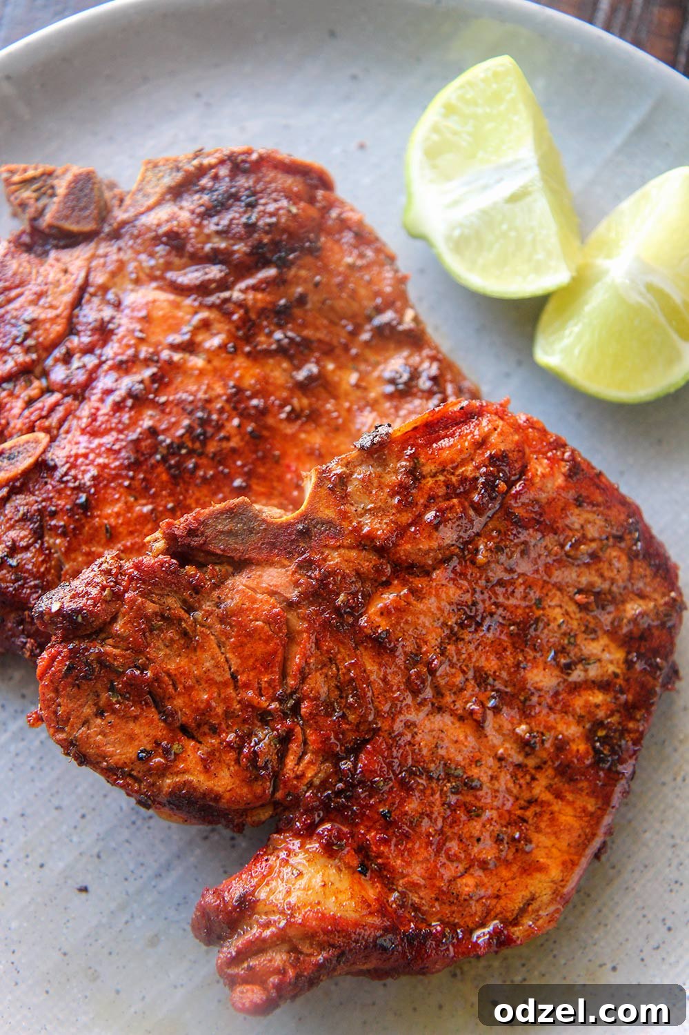 Crispy Golden Pork Chops 2 Two golden-brown chuletas fritas on a gray plate, garnished with two fresh lime wedges.