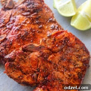 two chuletas fritas on a gray plate with two lime wedges.