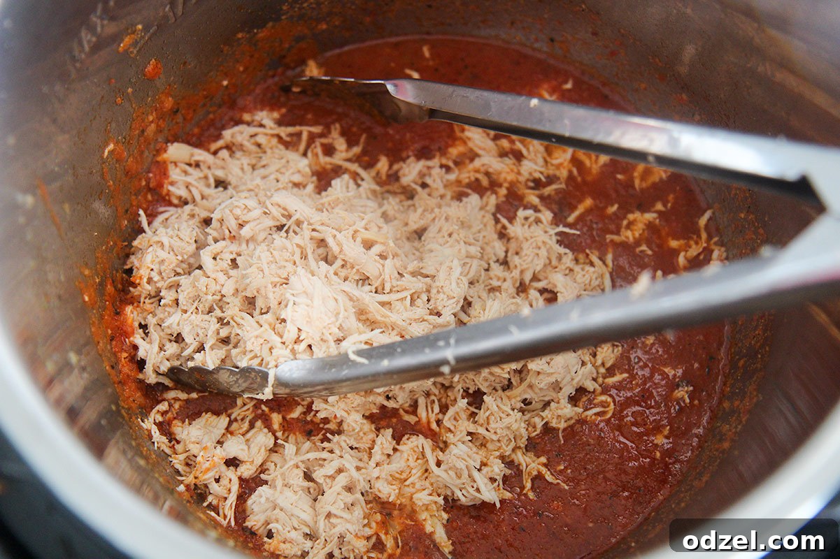 Smoky Instant Pot Chicken Tinga 4 shredded white meat chicken and red sauce in the instant pot with some tongs.