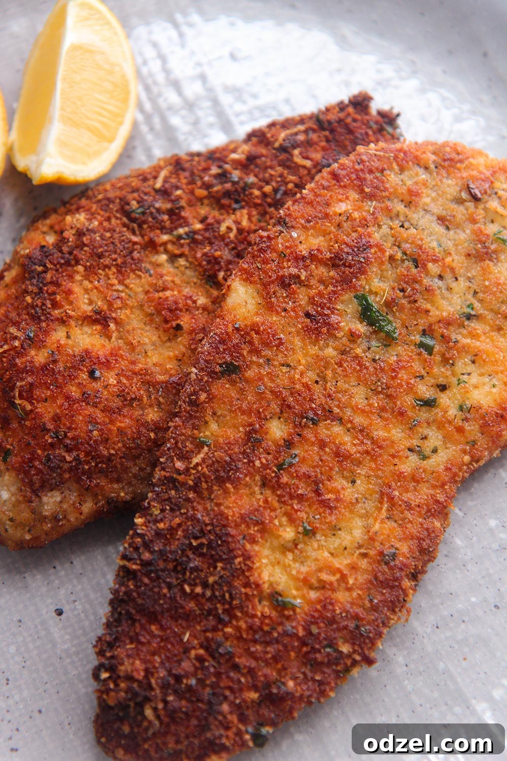 Golden Crunchy Chicken Cutlets 2 Two golden-brown crispy chicken cutlets with a fresh lemon wedge, ready to be served on a white plate.