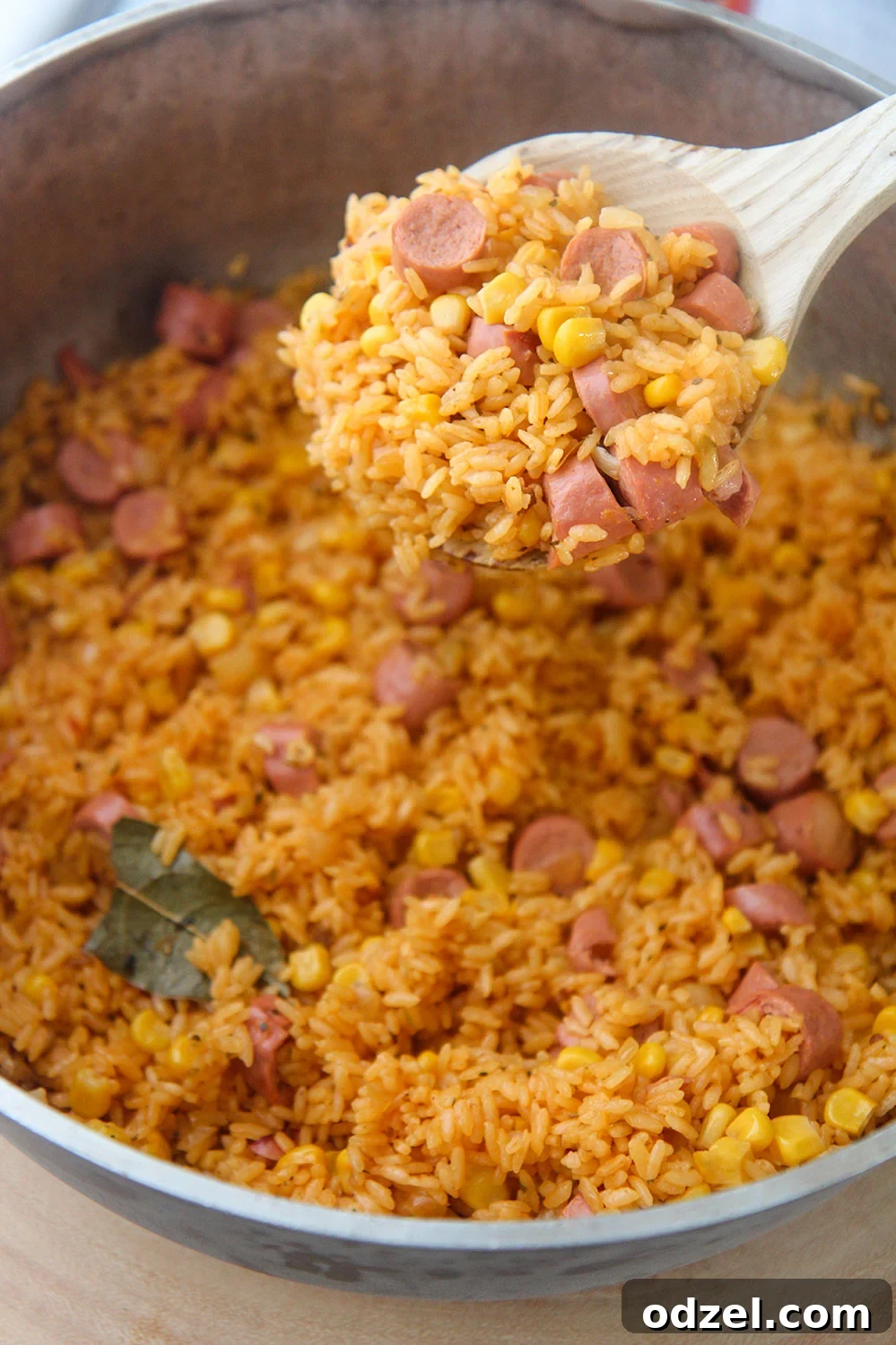 A wooden spoon filled with vibrant yellow Arroz con Salchichas, highlighting the sausage and corn.