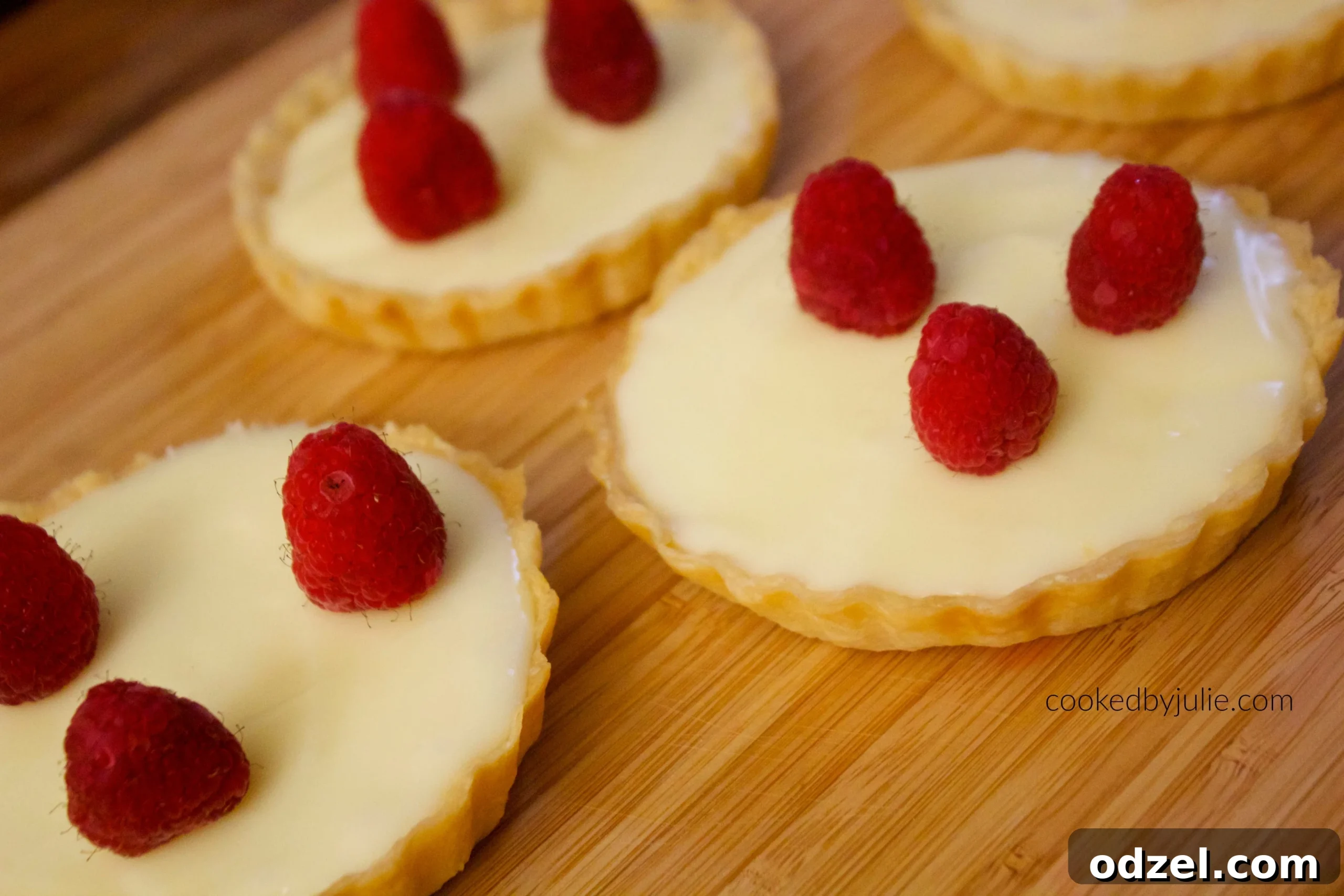 Decadent White Chocolate Tartlets 2 Two beautifully arranged white chocolate tarts topped with fresh raspberries, seen from an overhead angle.