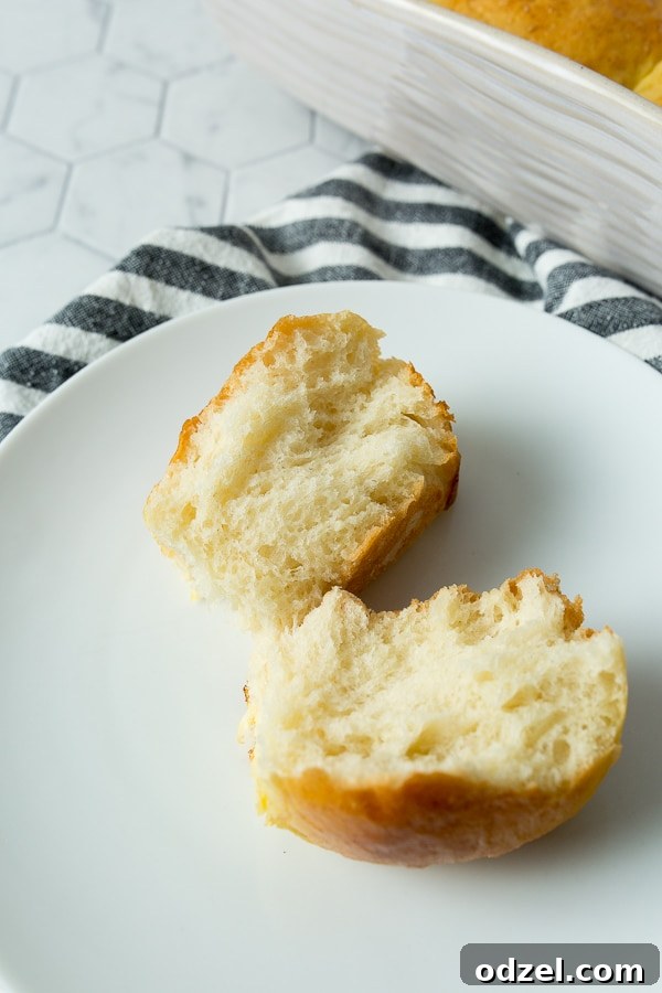 Pillowy Homemade Dinner Rolls 4 one bread roll split in half on a small white plate with a blue and towel on the side.