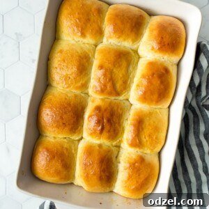a dozen baked dinner rolls in a white baking dish on top of a white and blue kitchen towel.