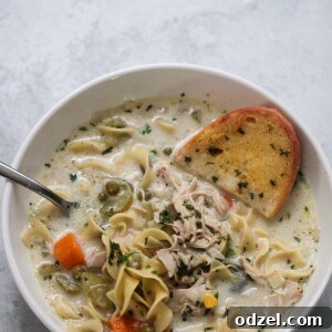 creamy chicken noodle soup in a bowl with a spoon and slice of garlic bread.
