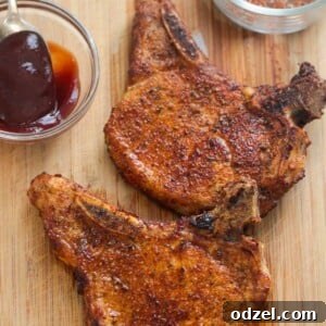 Two air fried bone-in pork chops on a wooden board with barbecue sauce and a spice rub on the side.