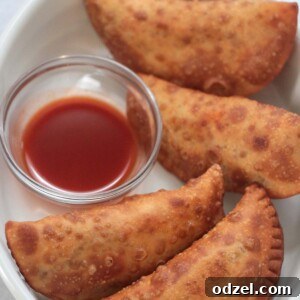 Four spicy beef and cheese empanadas with hot sauce on the side.