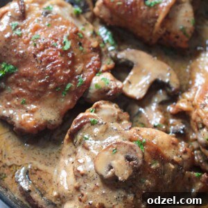 Champagne chicken in a skillet with cream sauce, mushrooms, and parsley.