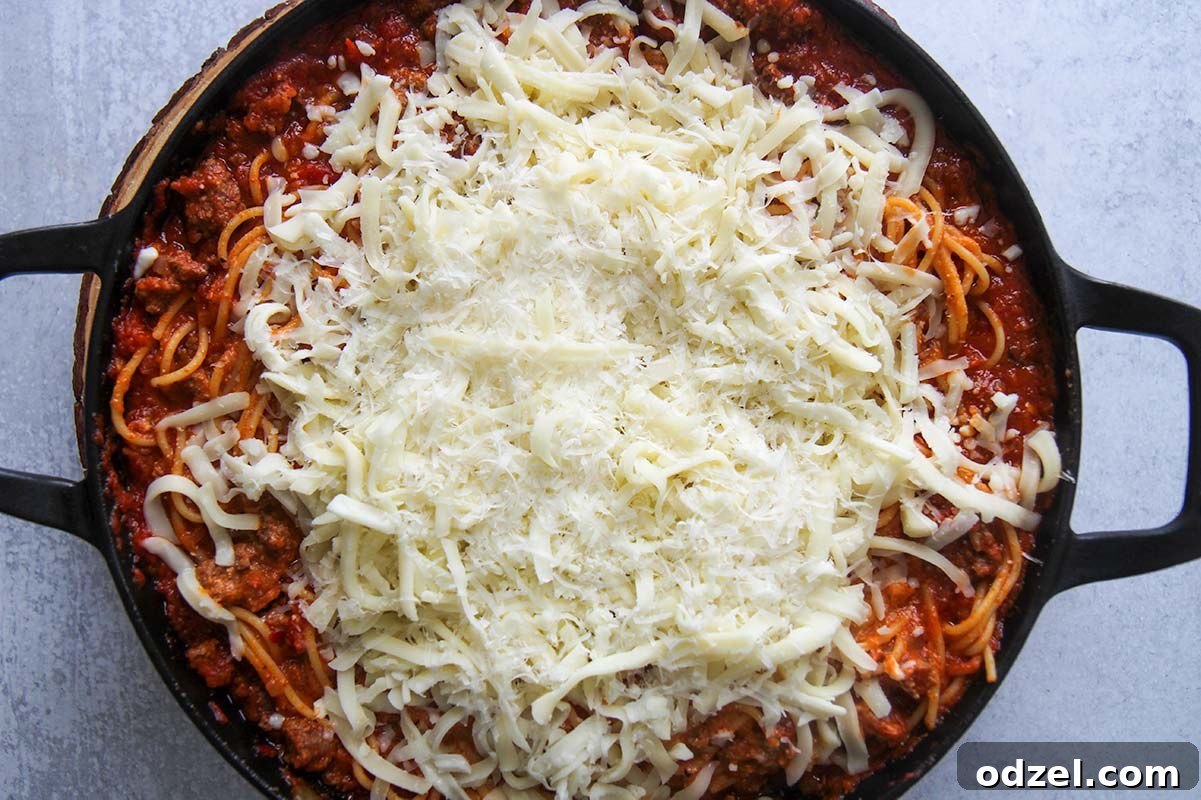 Close-up of baked spaghetti with a rich meat sauce and shredded mozzarella cheese on top, before baking.