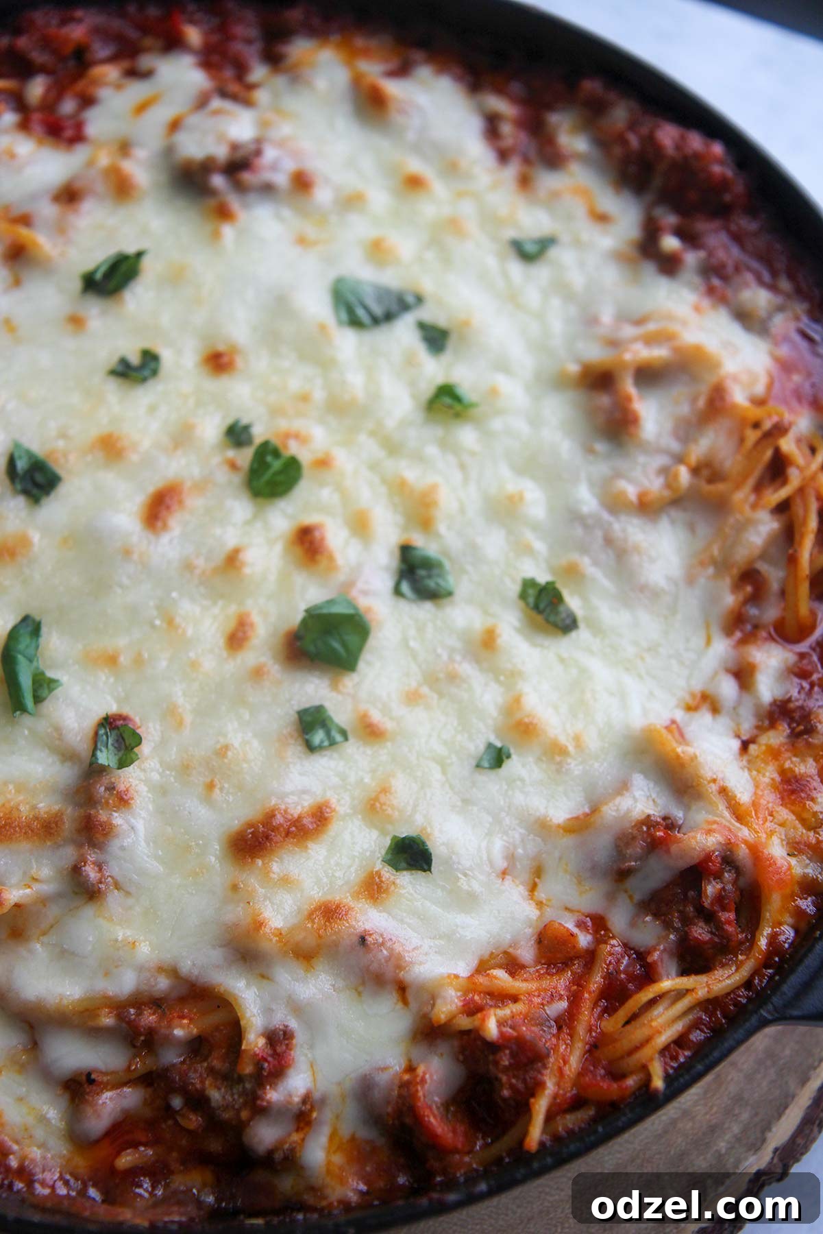 Close-up of baked spaghetti with golden melted cheese and fresh basil garnish, showing the bubbly crust.