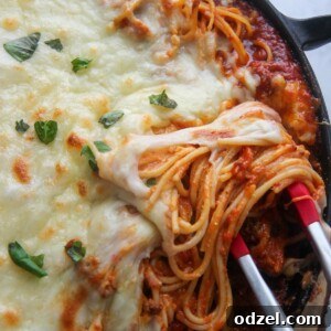 baked spaghetti in a cast iron skillet with tongs.
